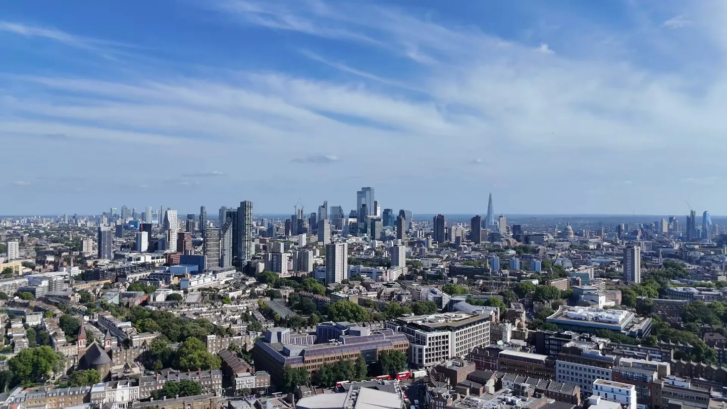 Drone view south across Islington and Clerkenwell towards the City of London, with the Shard and St Paul’s Cathedral on the skyline under a bright blue sky